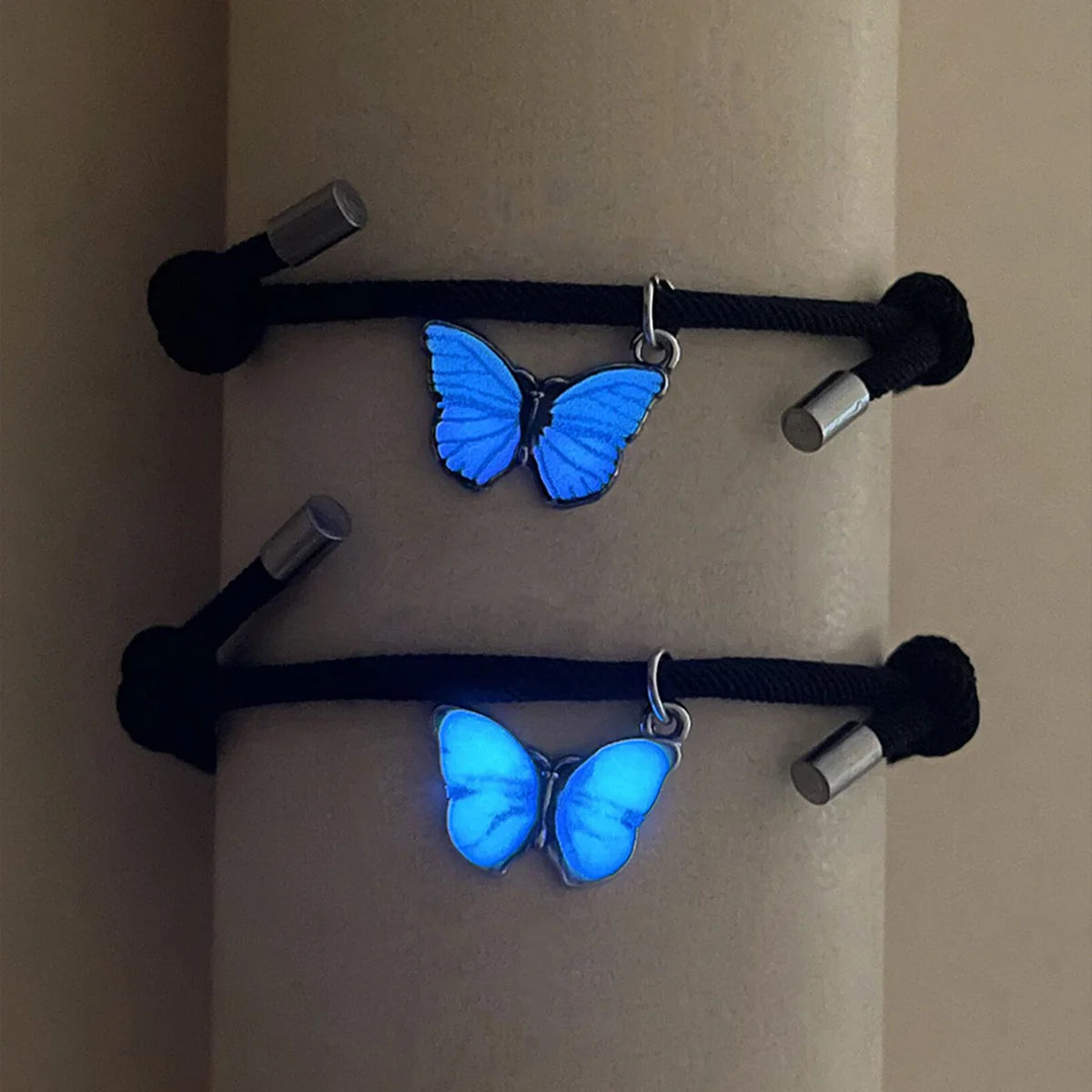 Two blue butterfly-shaped charms on black cords against a beige background