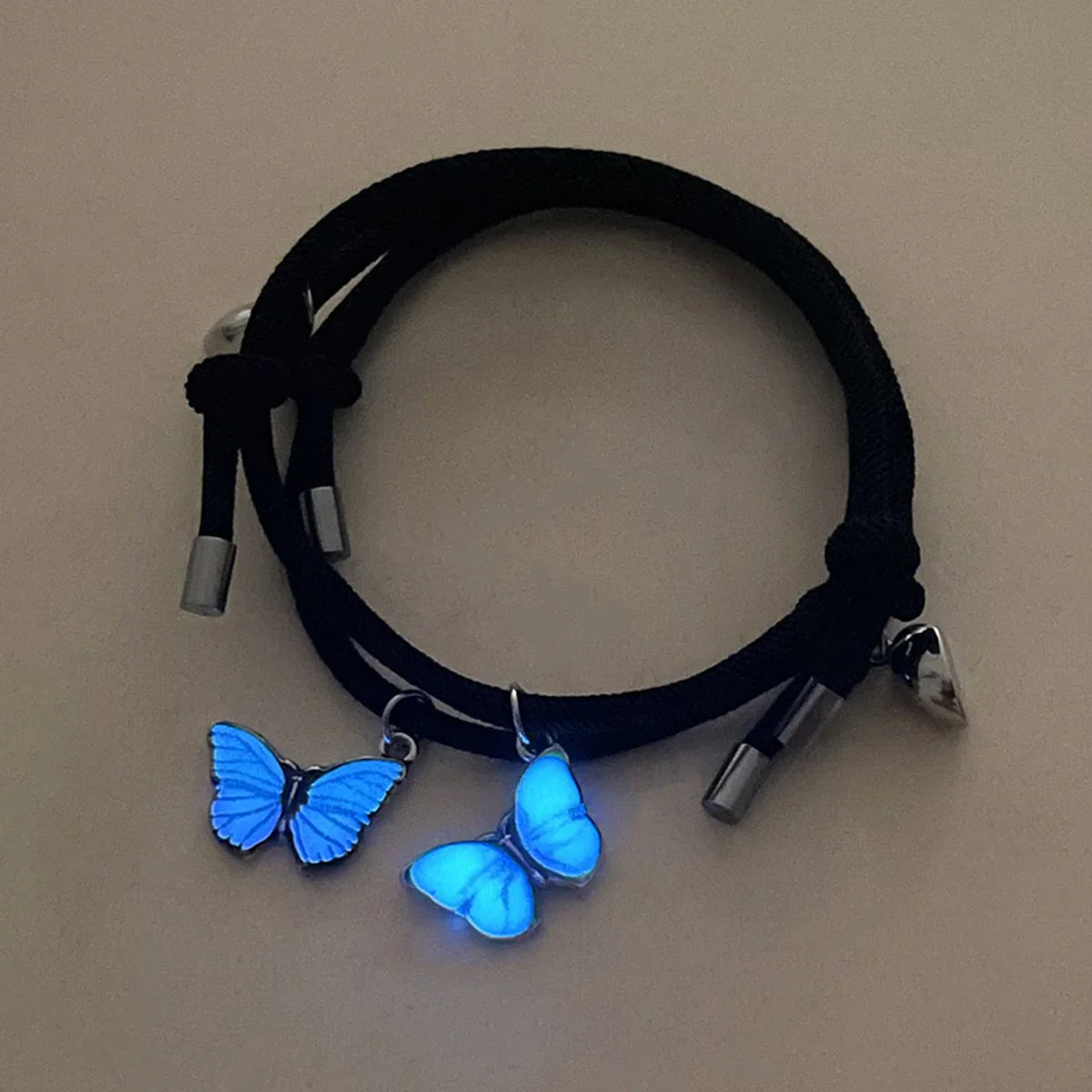 Black cord bracelet with glowing blue butterfly charms on a beige background