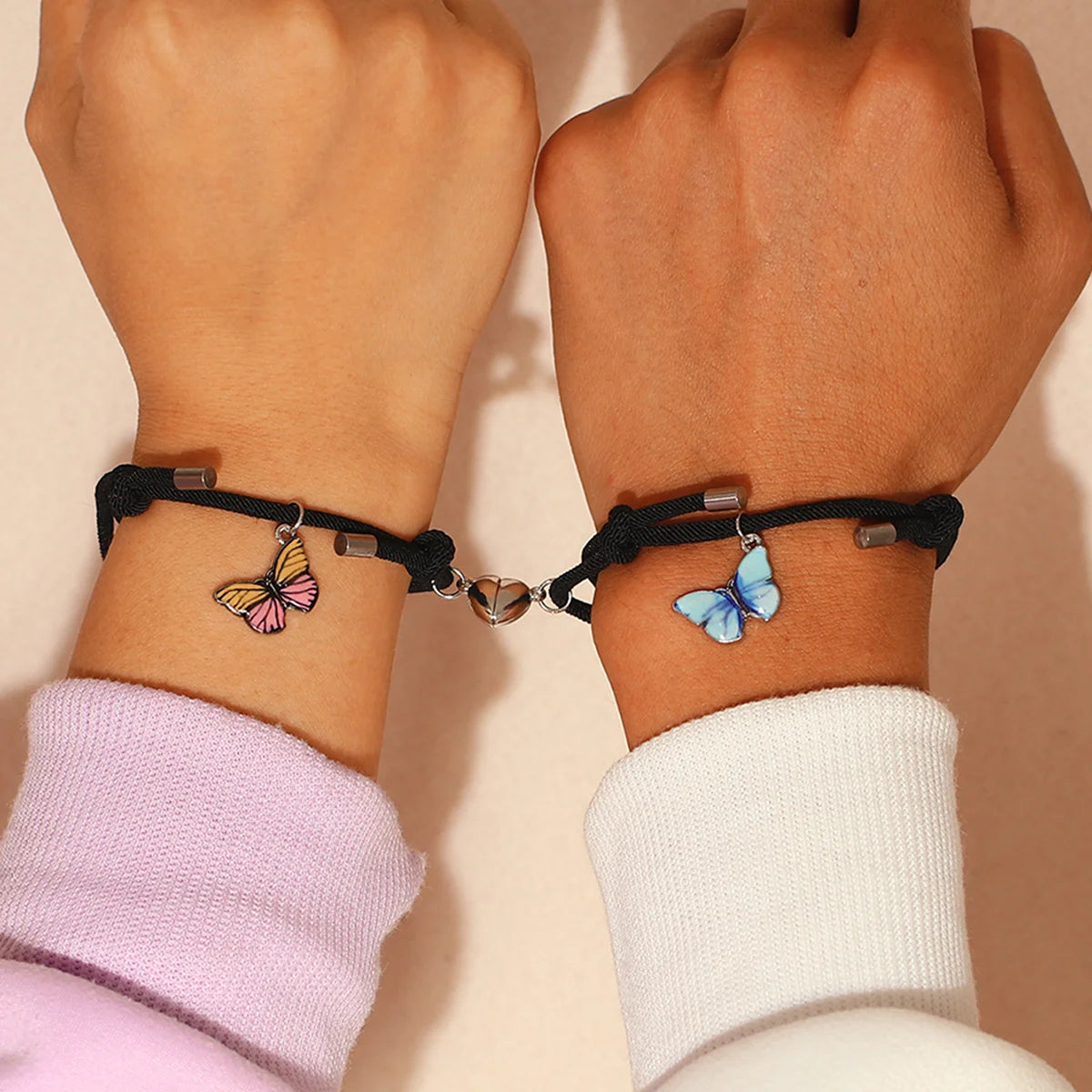 Two hands wearing black bracelets with butterfly charms on a beige background