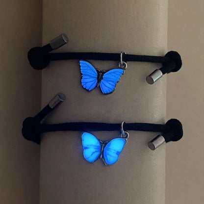Two blue butterfly-shaped charms on black cords against a beige background